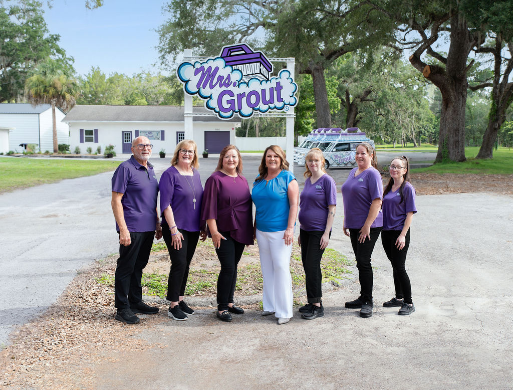 Mrs. Grout leadership team standing together outdoors in front of a branded company sign and service van. The image highlights the people behind Mrs. Grout and their commitment to serving the community.