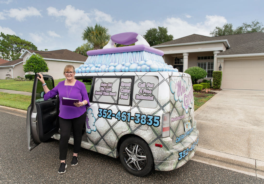 Mrs. Grout team member standing beside a branded service vehicle parked in front of a customer's home. The image highlights the company's mobile tile and grout restoration services delivered directly to homeowners.