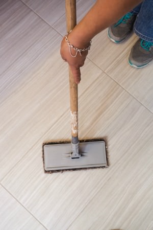 someone removing dirt from tile before moping