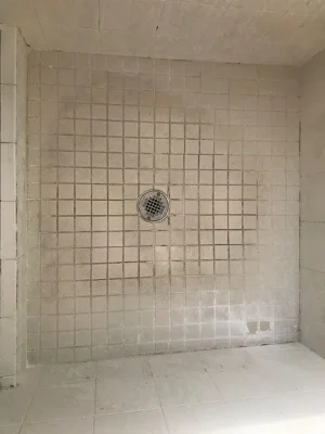 Accessible roll-in shower with tiled walls and floor, a wall drain, and visible discoloration and staining on the tile and grout.